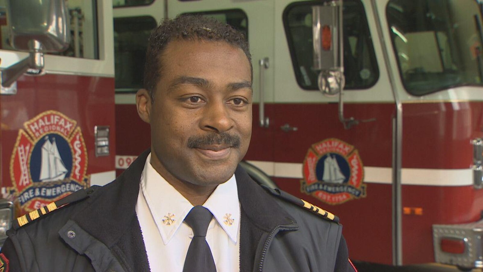 Corey Beals souriant devant des camions de lutte contre les incendies