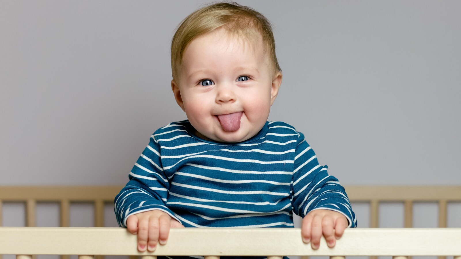 Un bébé debout dans son berceau qui grimace à la caméra