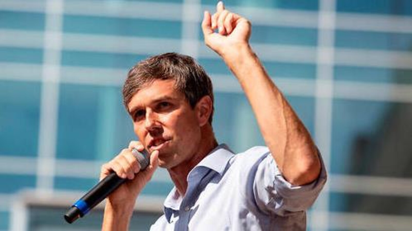 Beto O'Rourke tient un micro dans une main et lève l'autre main vers le ciel