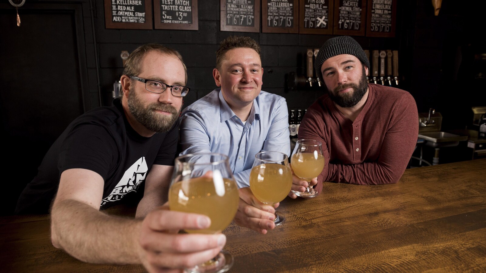 Trois hommes posent avec trois verres de bière.