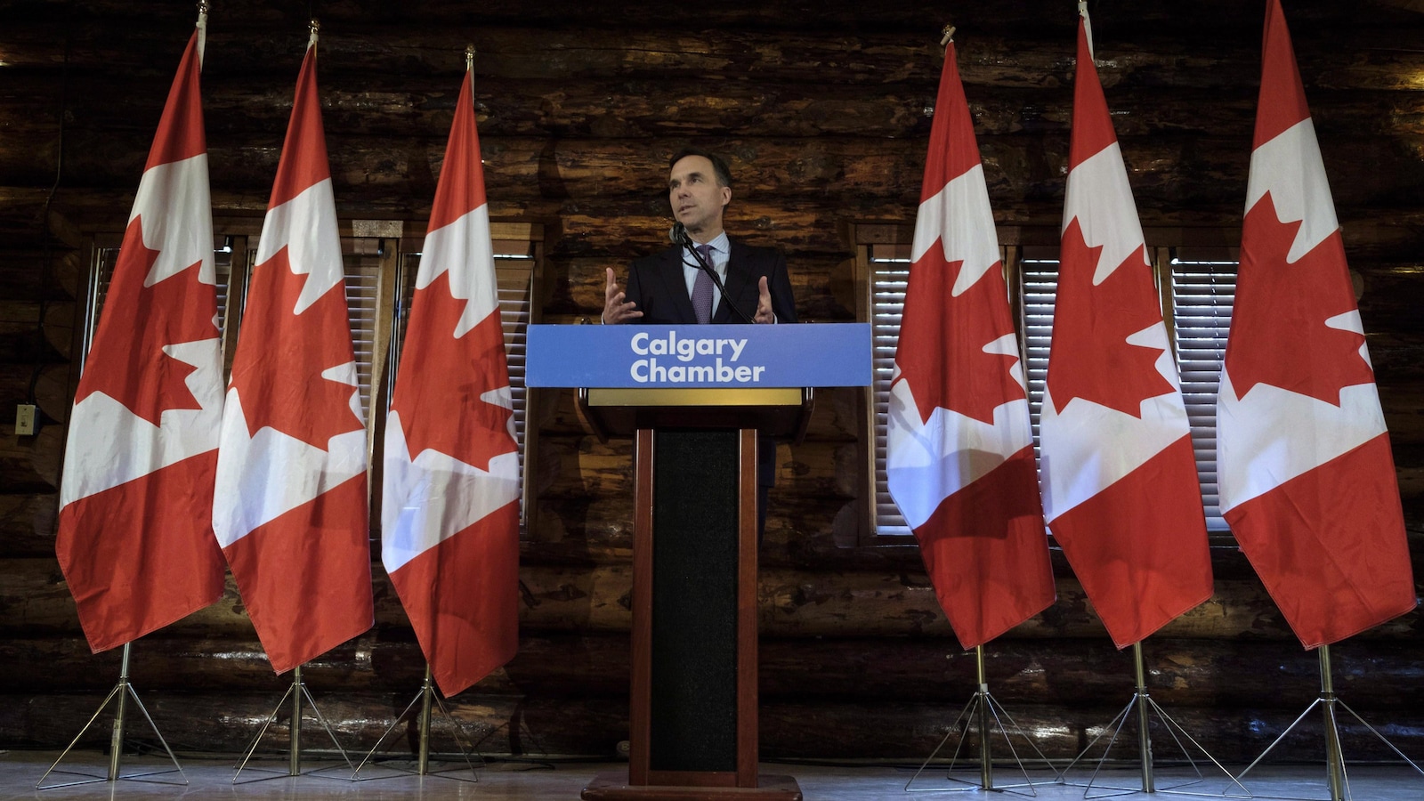 Bill Morneau en conférence de presse entouré de drapeau canadiens