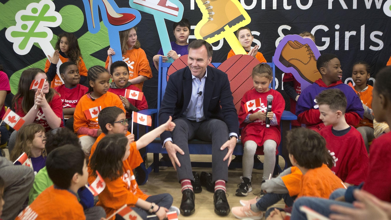 Le ministre Morneau est entouré d'enfants et il essaie des souliers.