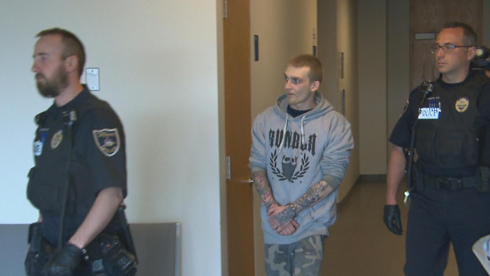Un homme menotté avance dans les couleurs du palais de justice de Chicoutimi. Il est accompagné par deux policiers.