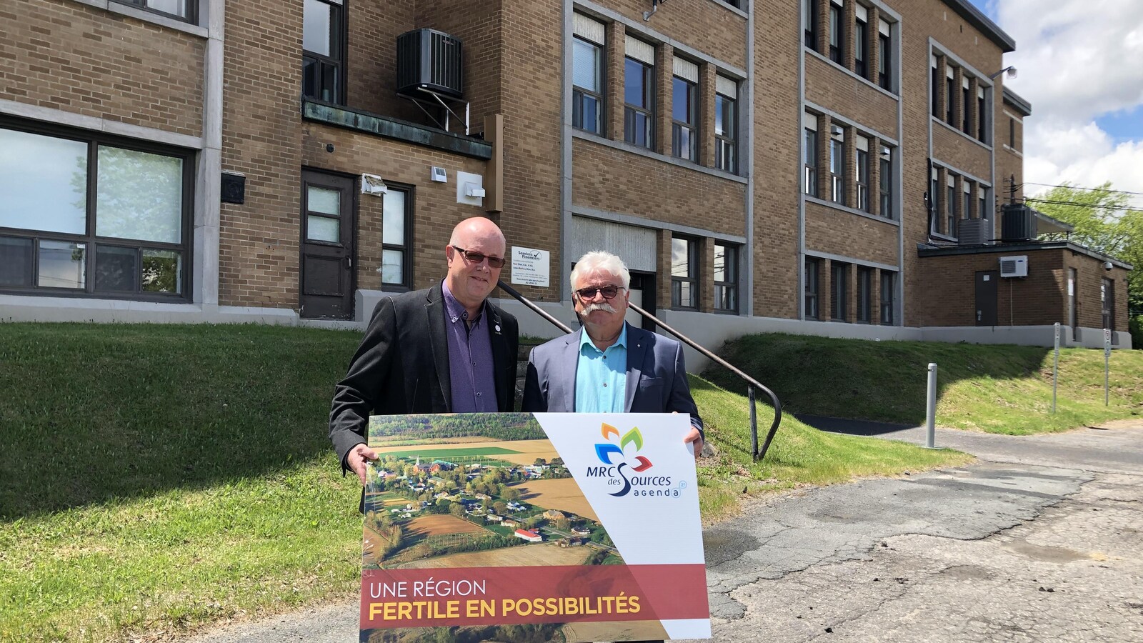 Deux hommes posent en tenant une affiche où il est écrit «une région fertile en possibilités»