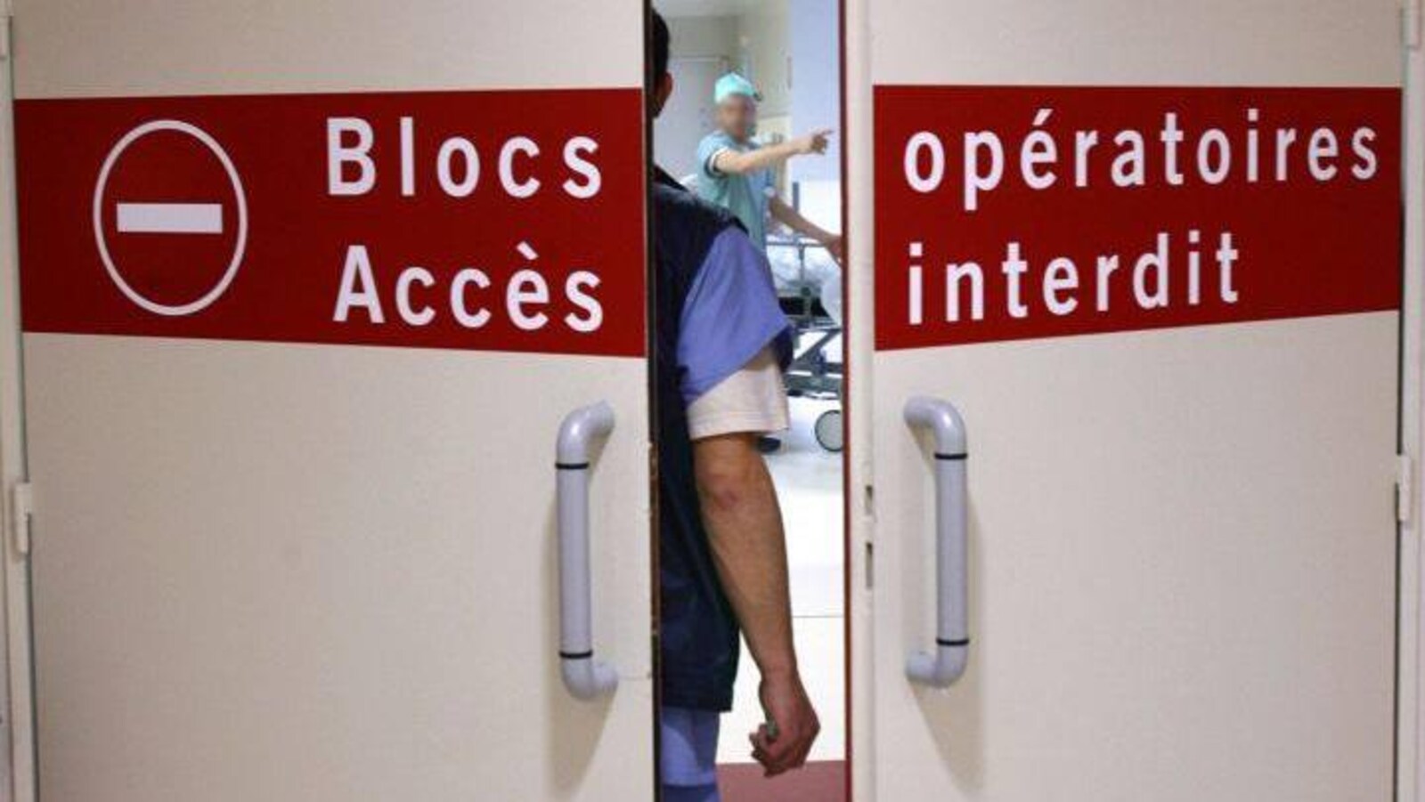 Porte entrouverte du bloc opératoire. On y voit un homme de dos face à un médecin.