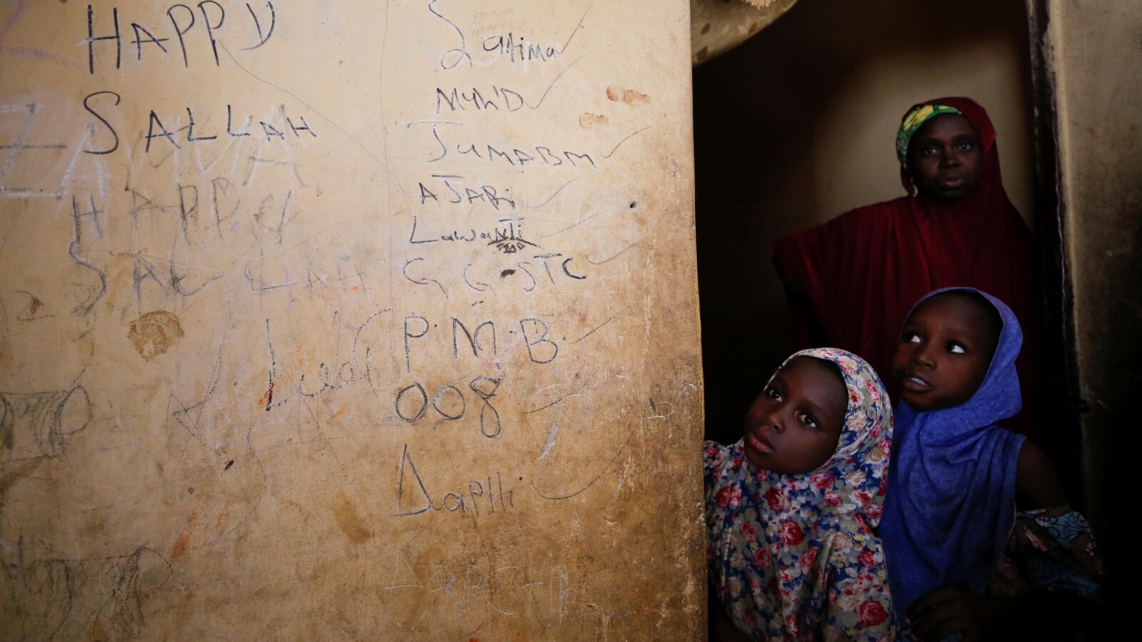 Deux fillettes nigériane voilées, accompagnées de leur mère, à la porte d'une salle de cours.
