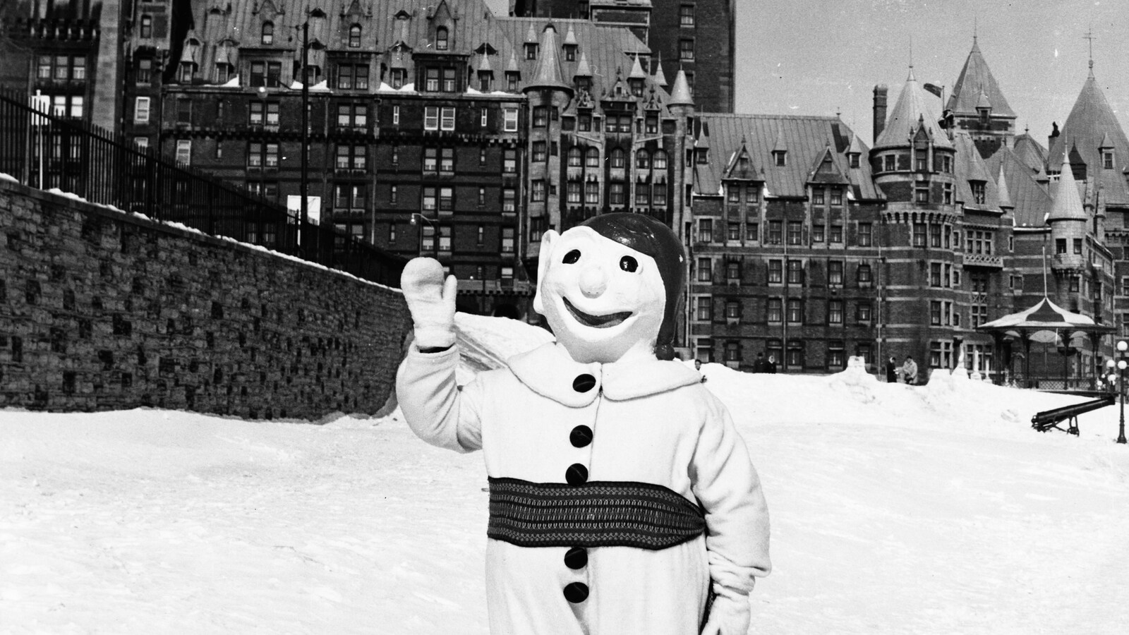 La mascotte se tient debout sur un sol enneigé, le Château Frontenac en arrière-plan.