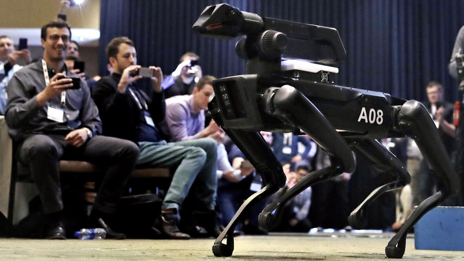Le robot à quatre pattes SpotMini marche dans une salle de conférence devant public durant un événement réunissant des professionnels de la robotique à Boston.