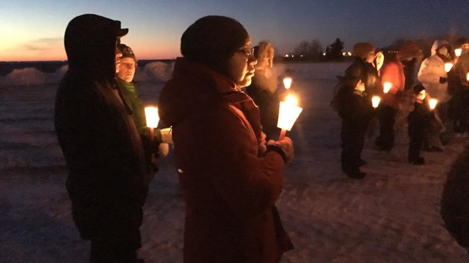 Une dizaine de personnes tiennent debout dans leurs mains des bougies à la tombée de la nuit.