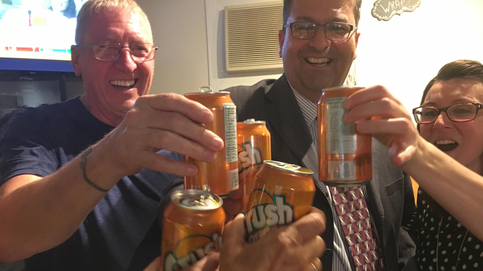 Trois personnes trinquent avec des canettes d'orangeade.