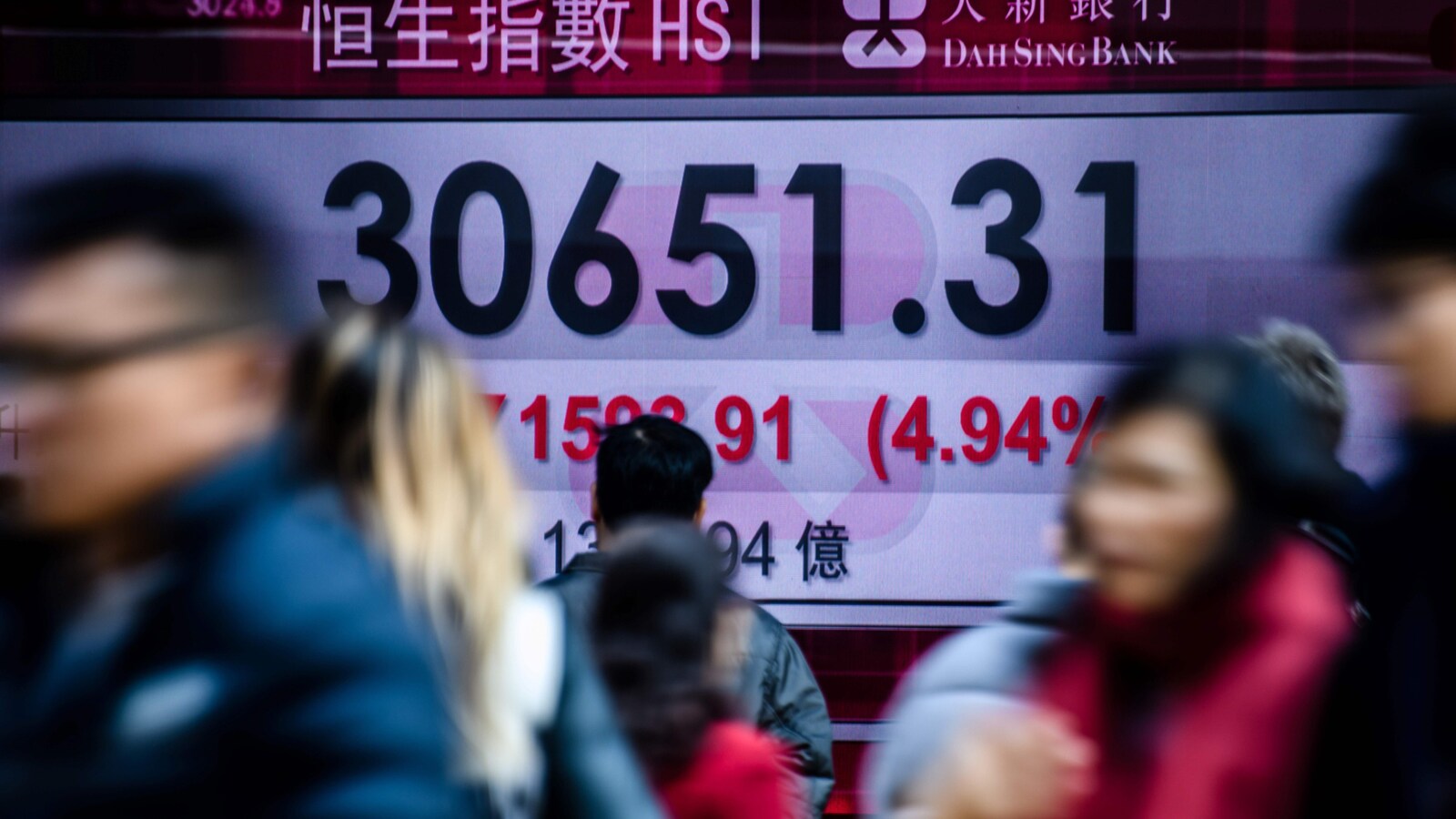Des passants marchent devant un écran qui indique la baisse de la Bourse de Hong Kong.