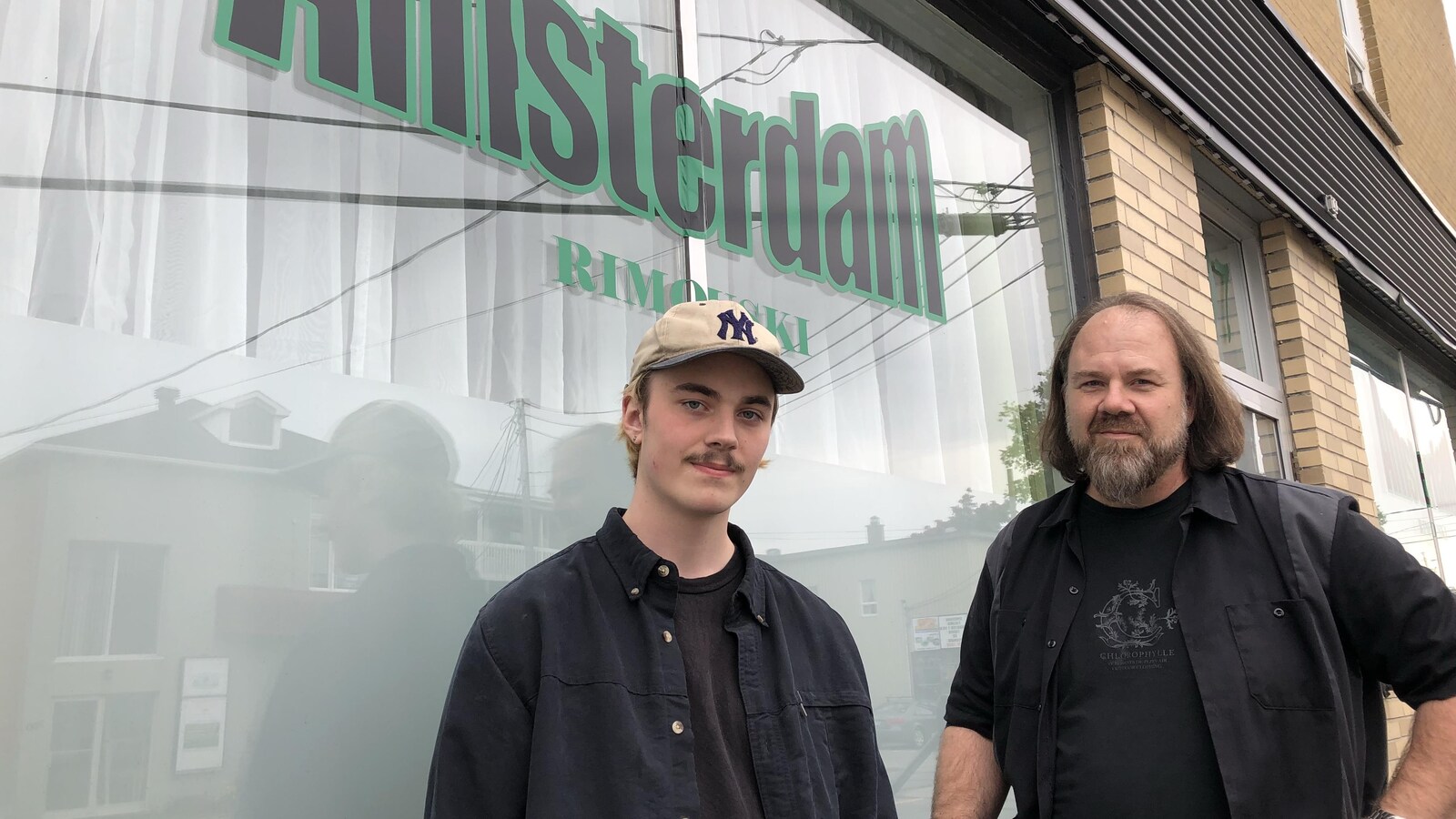 Ils prennent la pose devant la vitrine de leur boutique où on peut lire en noir et vert : Amsterdam Rimouski