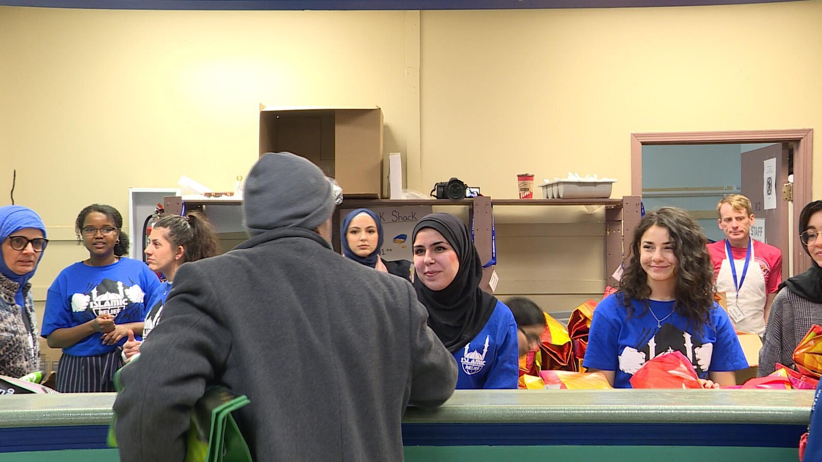 Des bénévoles d'Islamic Relief Canada, certaines portant le hijab, d'autres non, distribuent une trousse à un client du centre communautaire.