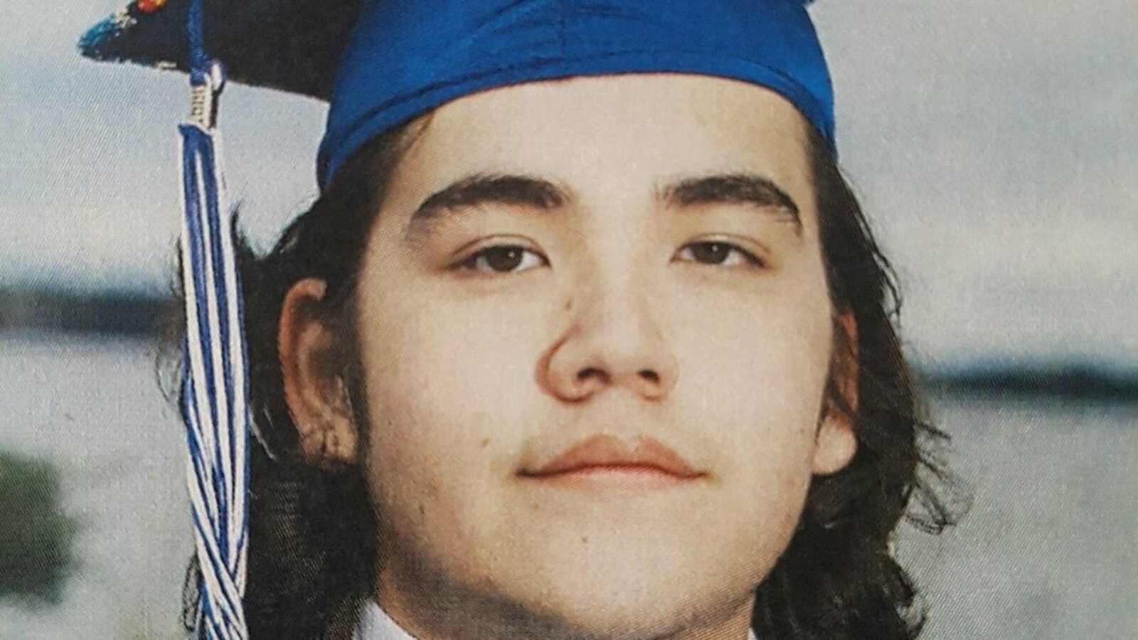 Le visage d'un jeune homme aux cheveux mi-longs, avec un chapeau de finissant.