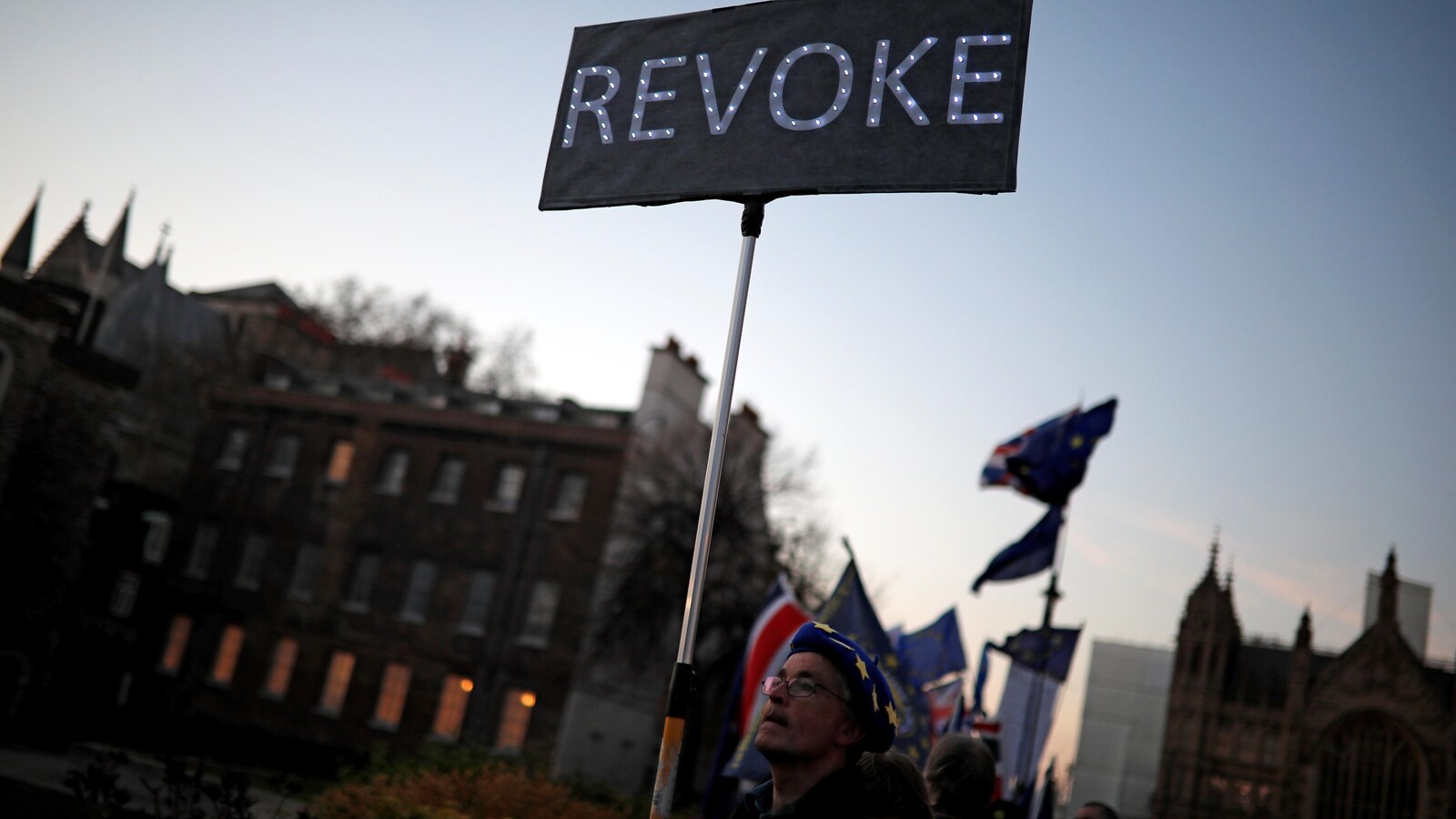 Un homme tient une pancarte sur laquelle est écrit : « revoke ».