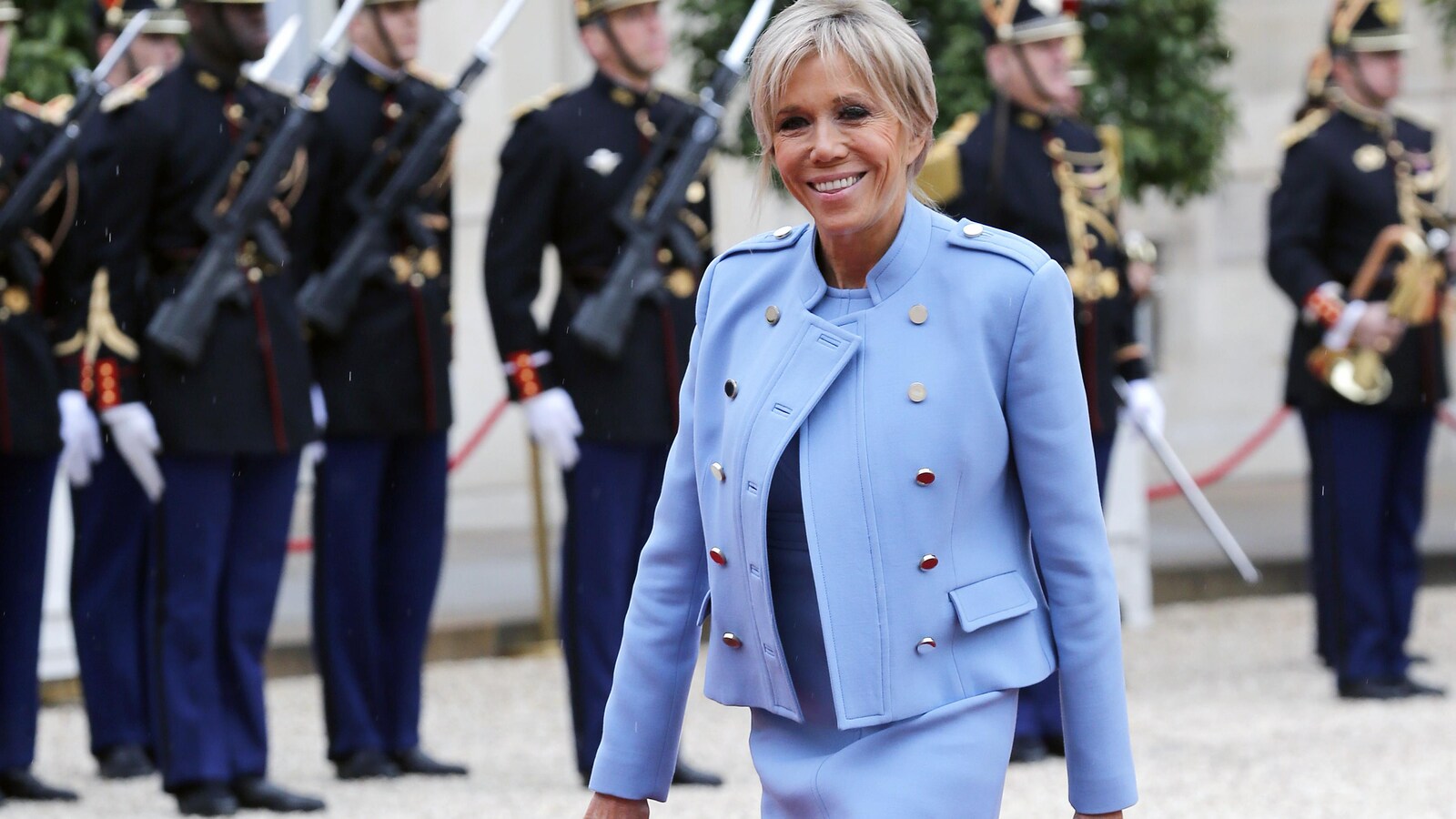 La première dame de France porte un ensemble bleu poudre et marche sur un tapis rouge tout en souriant aux photographes.
