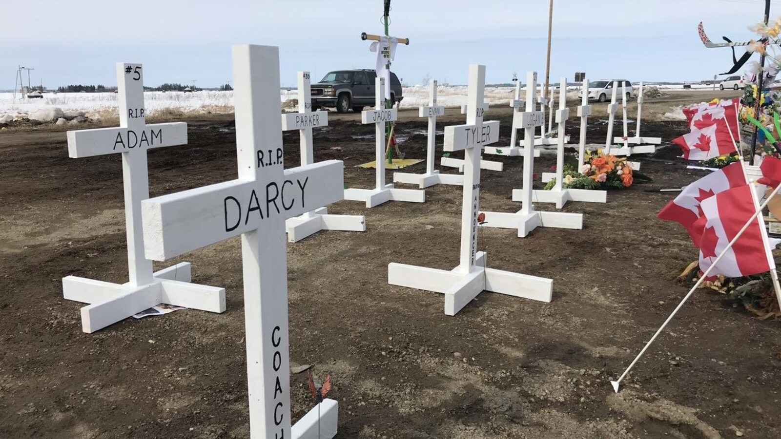 Croix en bois peintes en blanc portant le nom de chaque victime. déposées sur le sol.