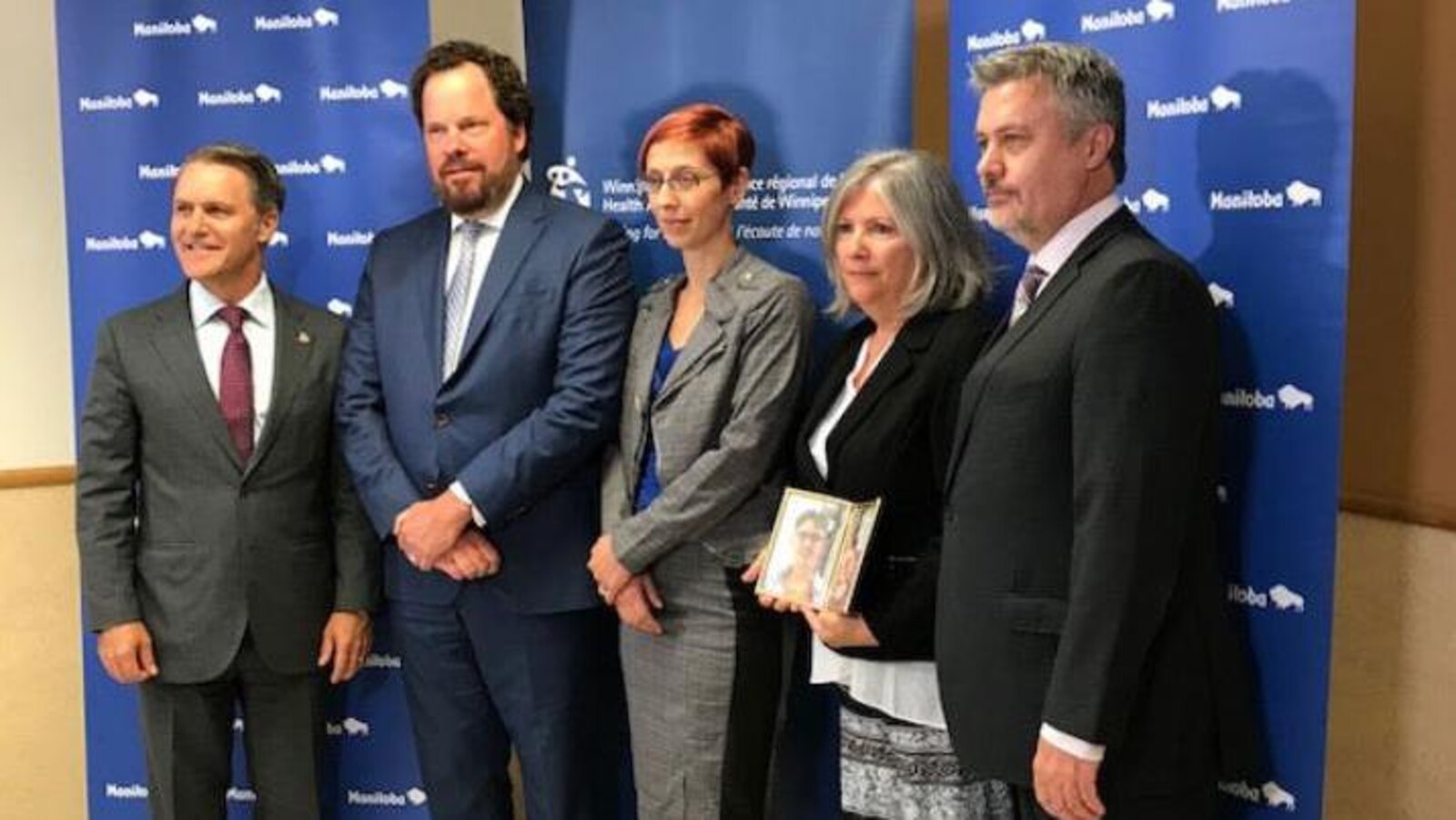 Cinq personnes sont debout et posent pour une photo. Le Dr Bruce Roe est le deuxième à partir de la gauche. Il porte un habit et croise les mains devant lui.