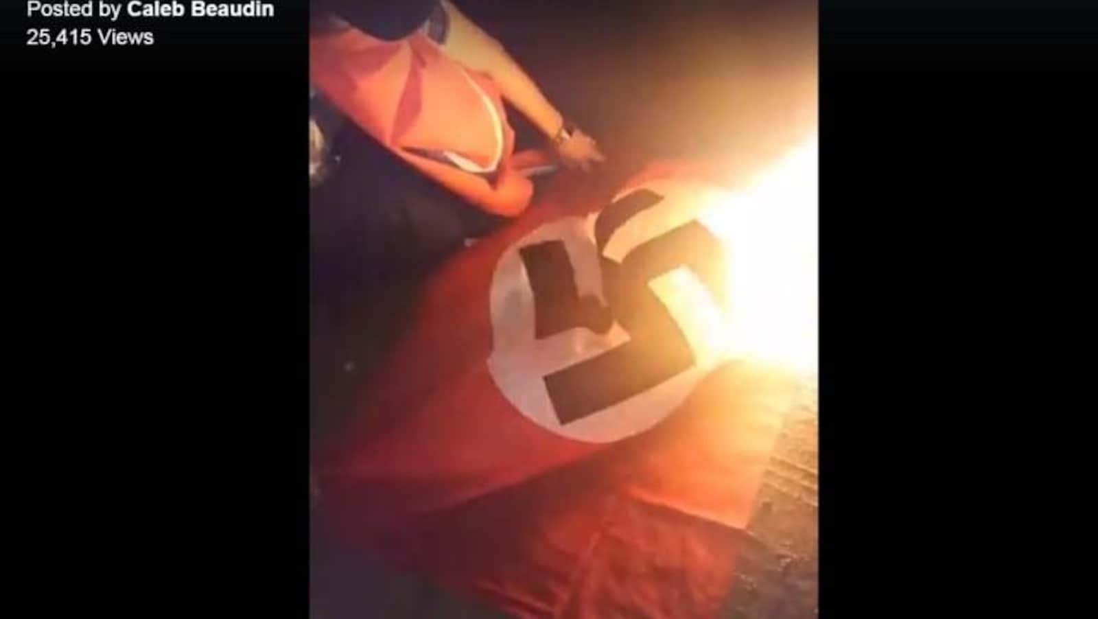 Un homme à genou à côté d’un drapeau nazi en train de brûler.