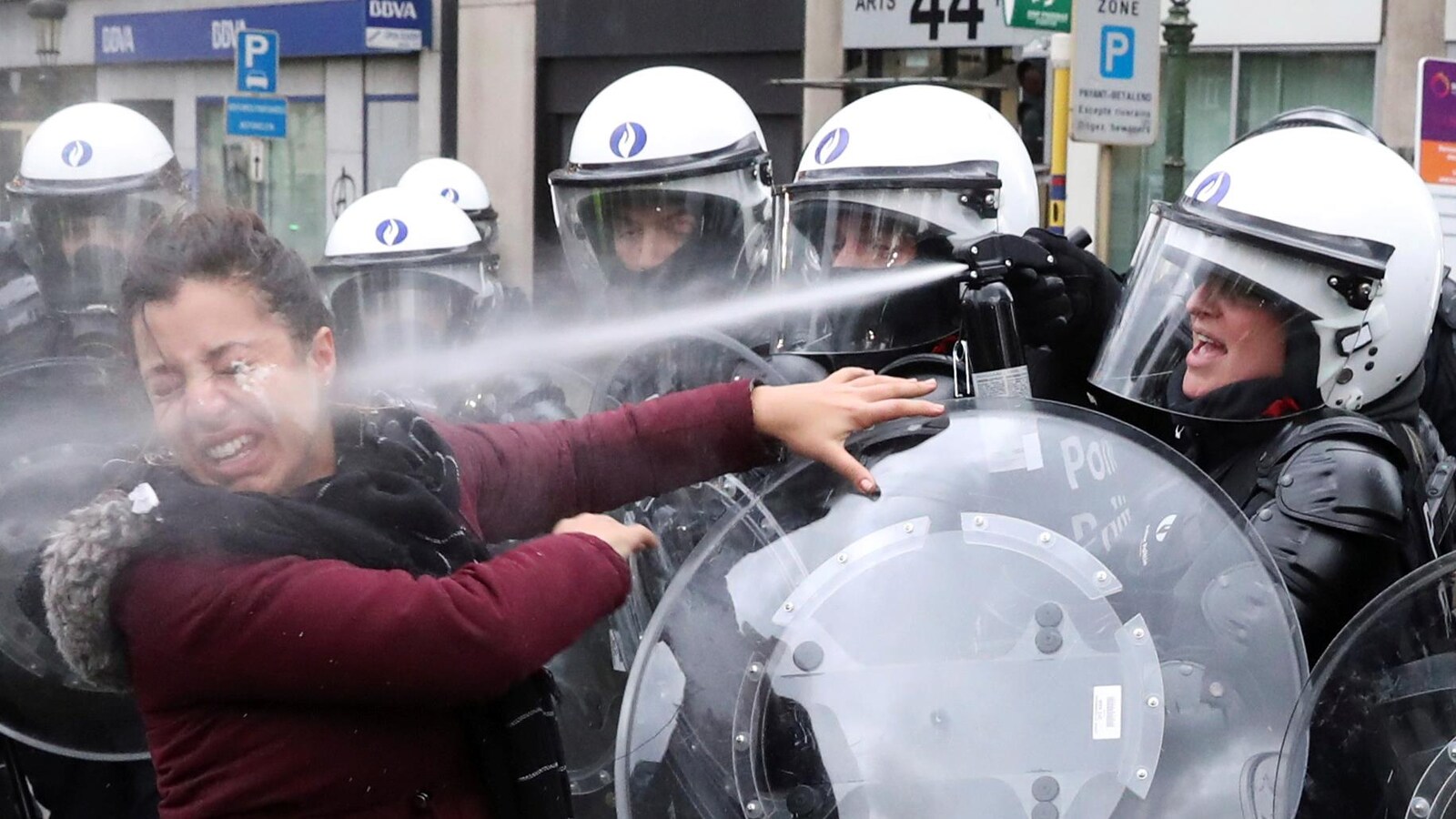 Une femme reçoit du gaz lacrymogène en pleine figure, lancé par une policière avec un bouclier.