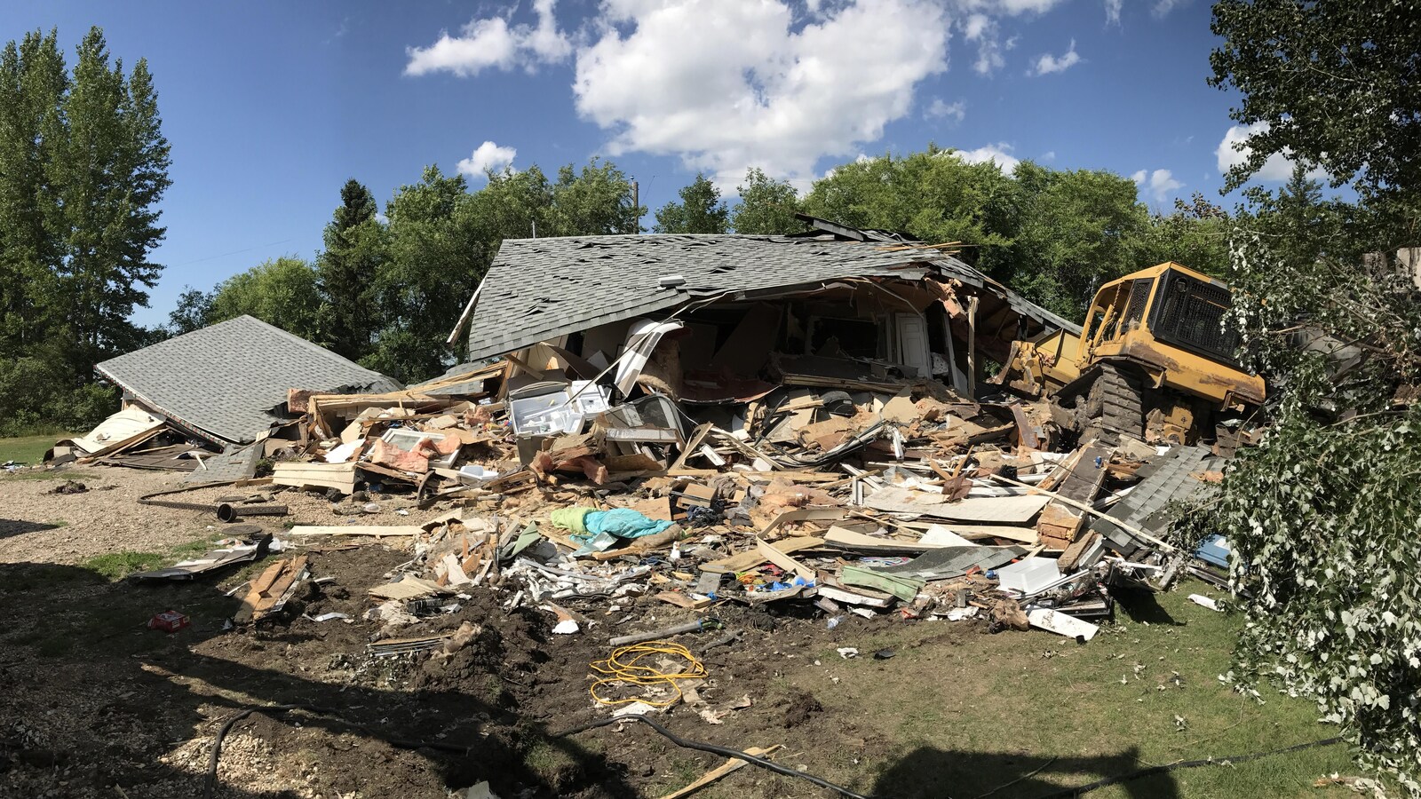 La maison semble avoir été complètement détruite par une tornade, sauf que le bulldozer qui l'a mise à terre se trouve juste à côté.