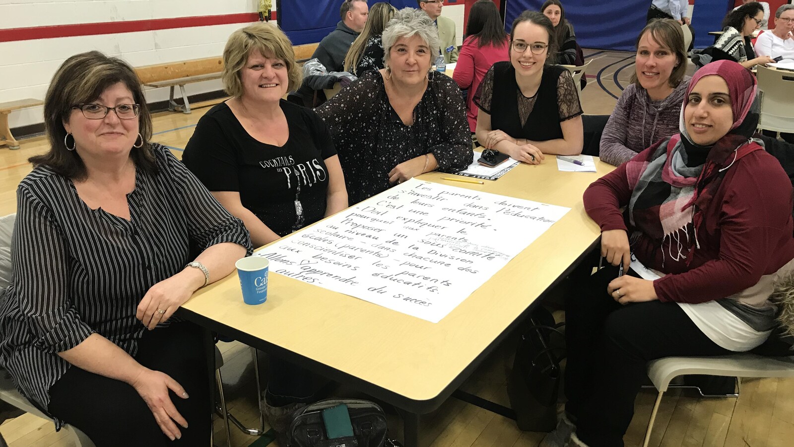Six femmes sont assises autour d'une table dans un gymnase converti en salle de conférence.