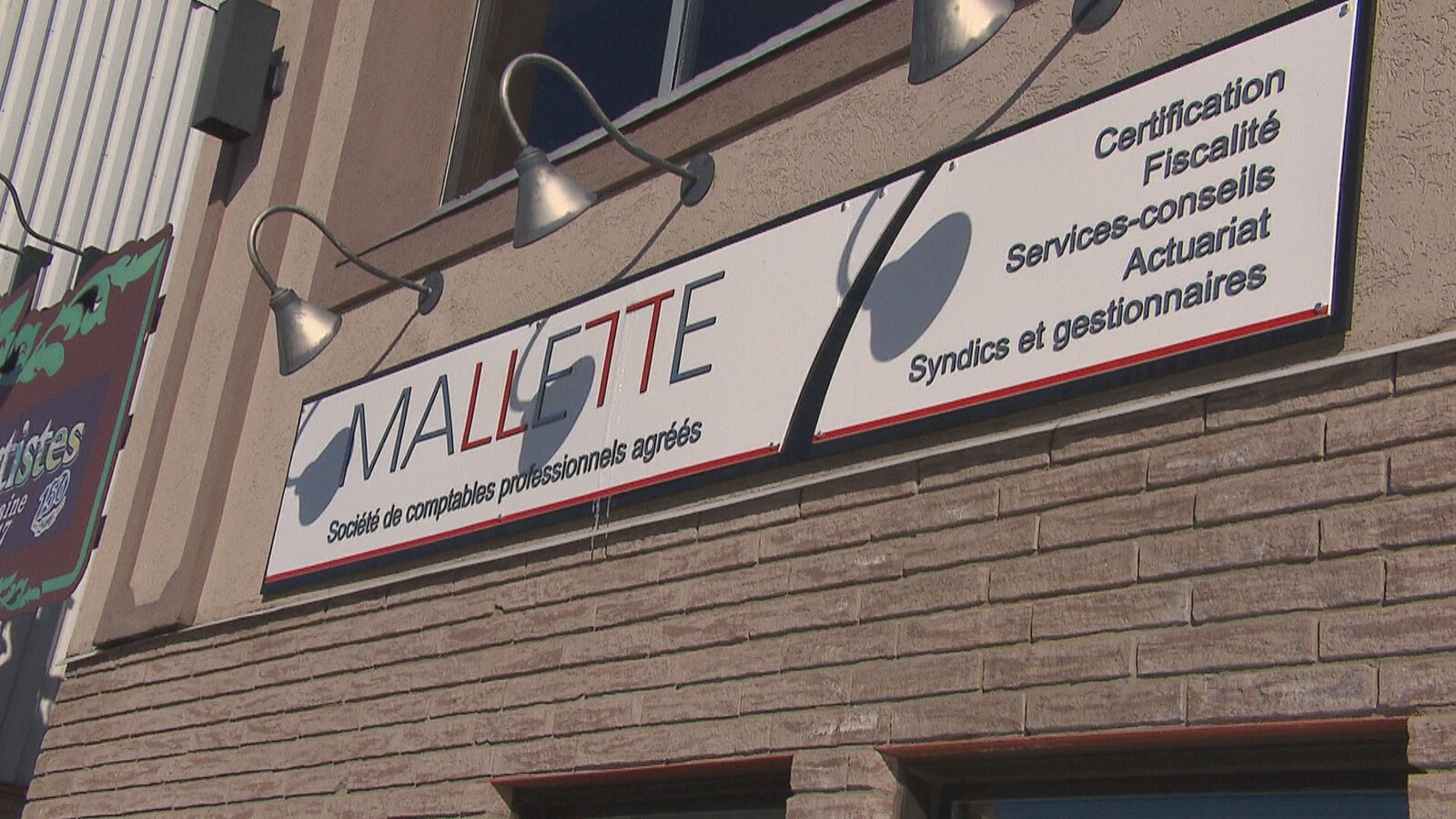 Une affiche indique le nom de l'entreprise sur un bâtiment de brique.
