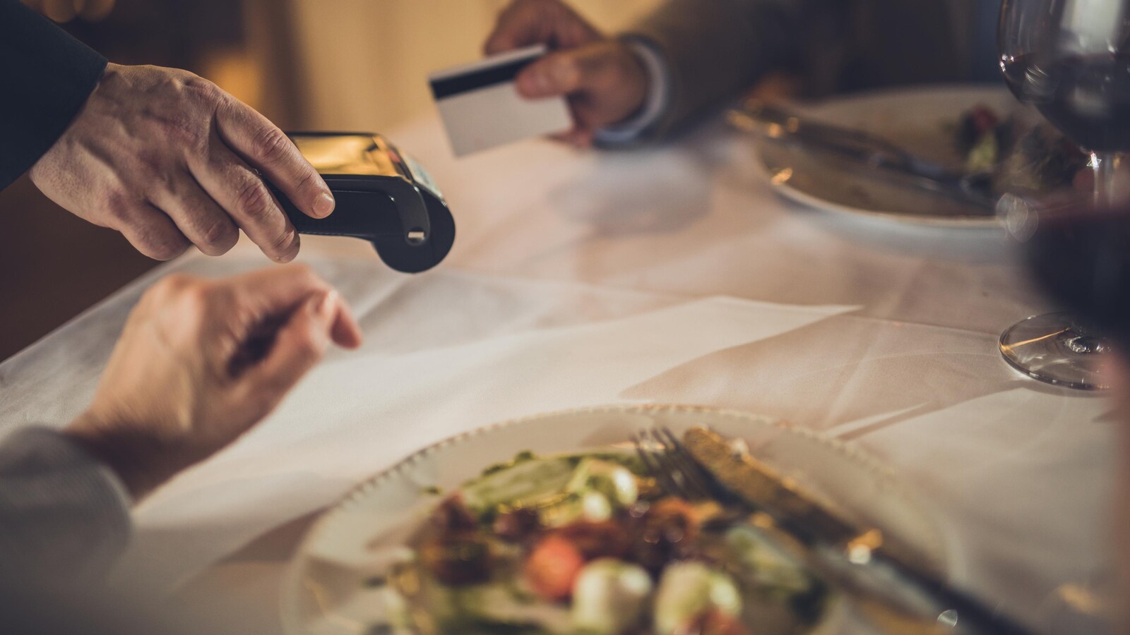 Une main avec une carte de crédit, une autre avec une machine interac, des assiette. Personne n'est reconnaissable.