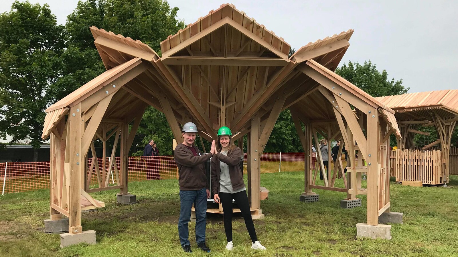 Un professeur et une étudiante se trouvent devant une structure en bois.
