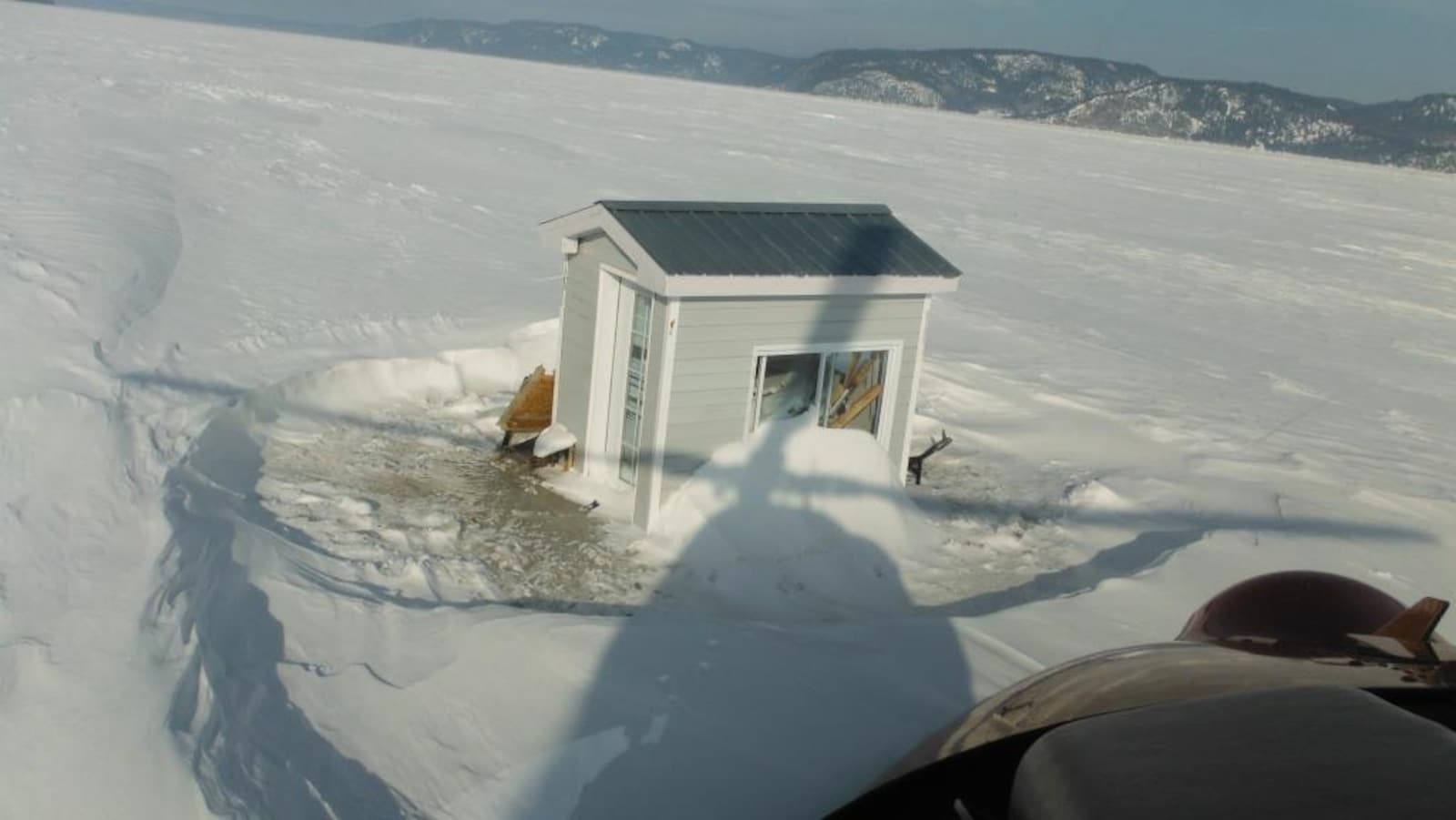 On voit une cabane à pêche prise dans une épaisse couche de glace.