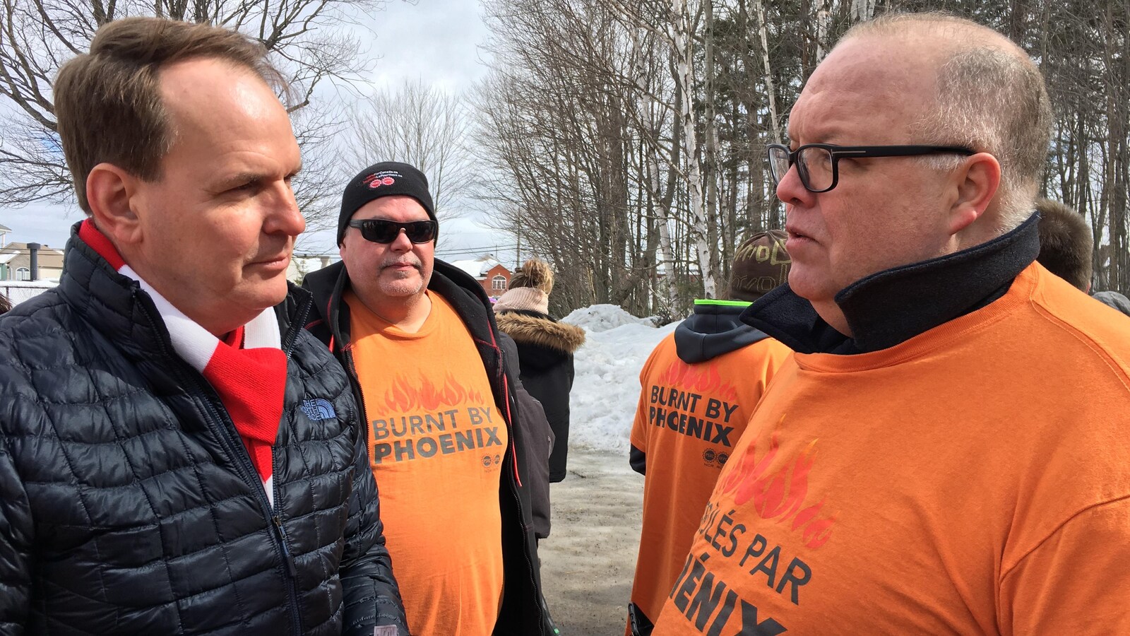 Steven MacKinnon parle avec un fonctionnaire fédéral vetû d'un gilet orange portant l'inscription «brûlés par Phénix».