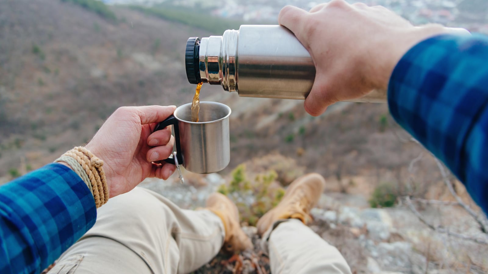 Un homme assis au sommet d'une montagne se verse une tasse de café.