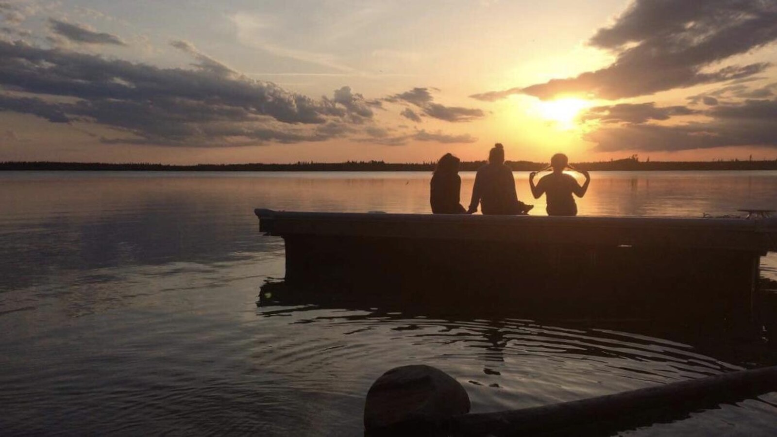 Des membres de la communauté de La Loche regardent le coucher de soleil devant le lac.