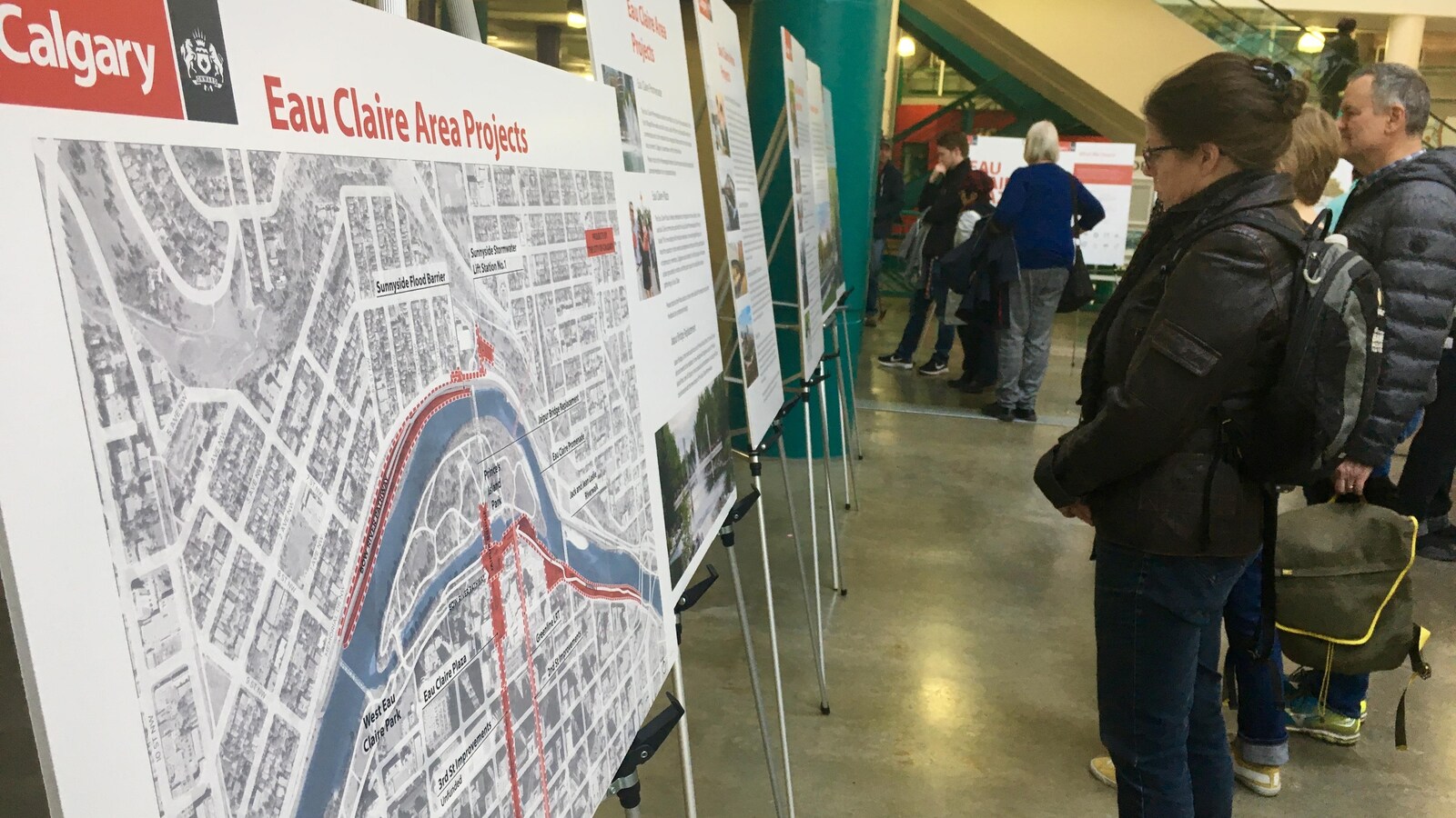 Une femme est debout devant des panneaux d'informations, dont le premier représente une carte d'une ville avec une rivière qui passe au milieu.