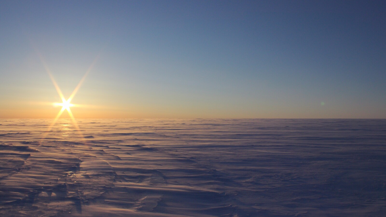 Un champ de neige à perte de vue, avec le soleil qui se couche en arrière-plan.