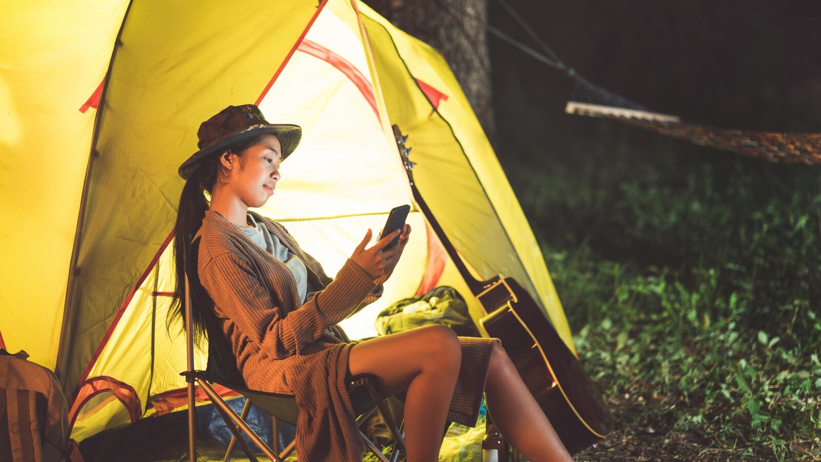 Une femme asiatique consulte son téléphone cellulaire en camping