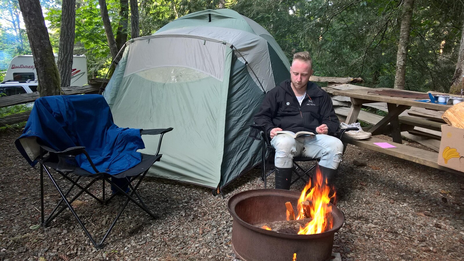 Un campeur sur l'île Salt Spring en Colombie-Britannique lit un livre entre sa tente et un feu de camp