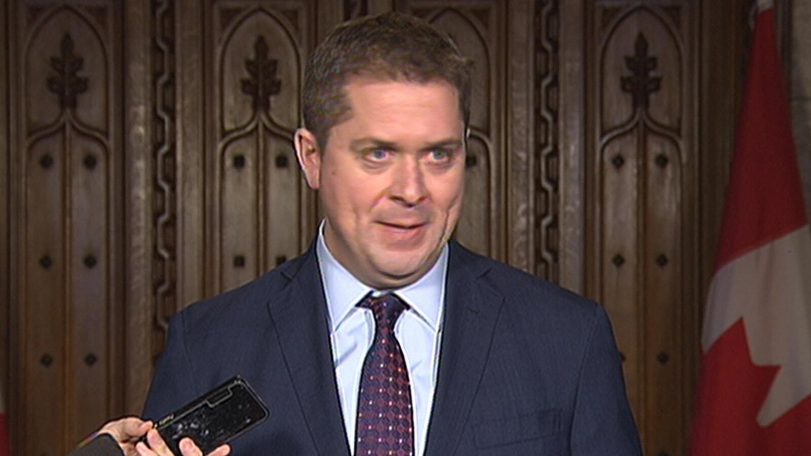 Andrew Scheer devant des drapeaux canadiens.