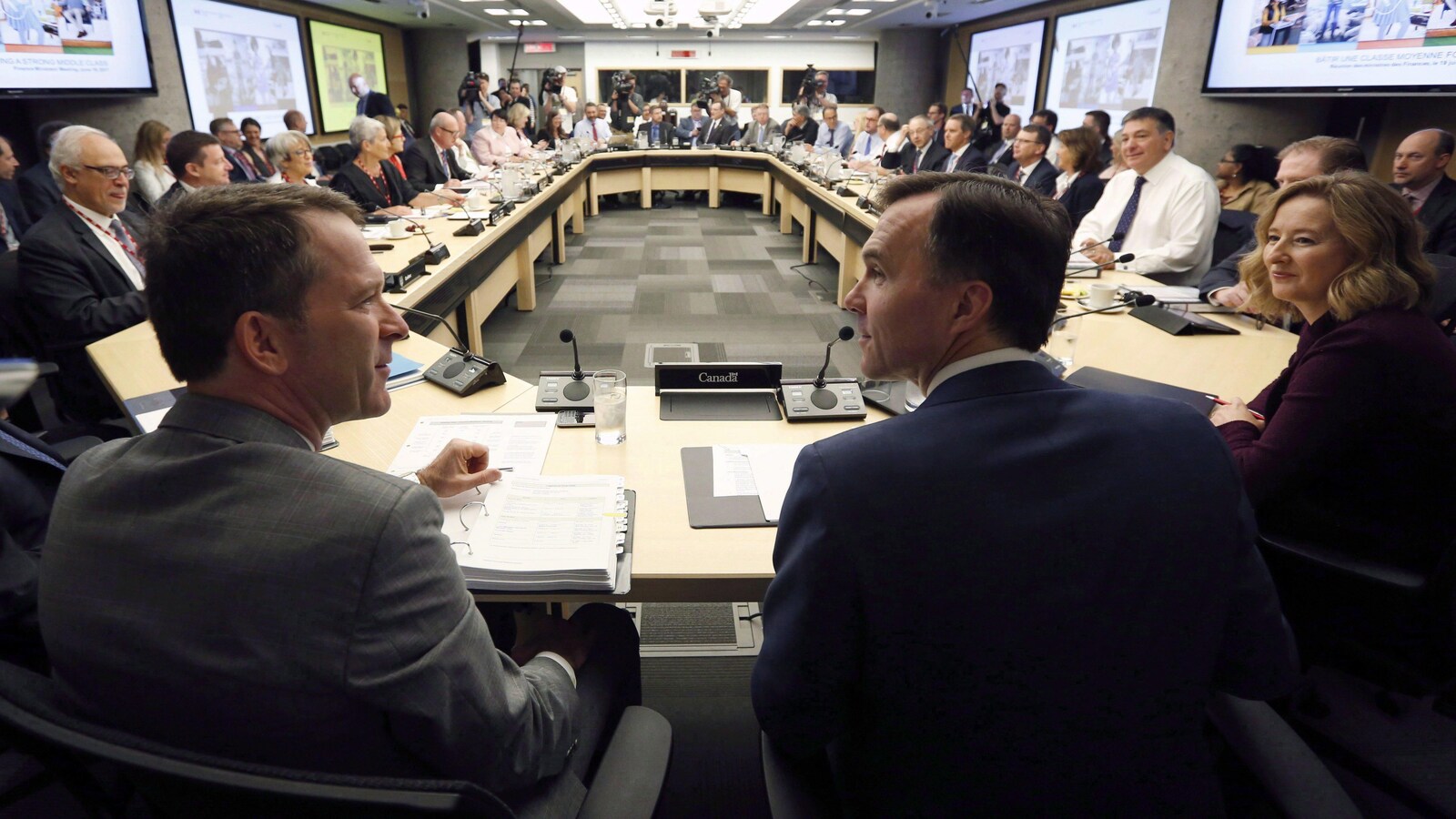 Les deux hommes se tiennent côte à côte, sous l'oeil de Carolyn Wilkins, de la Banque du Canada. Ils sont au premier plan. Dans la perspective, on peut discerner une trentaine de personnes réunies autour d'un bureau ovale.