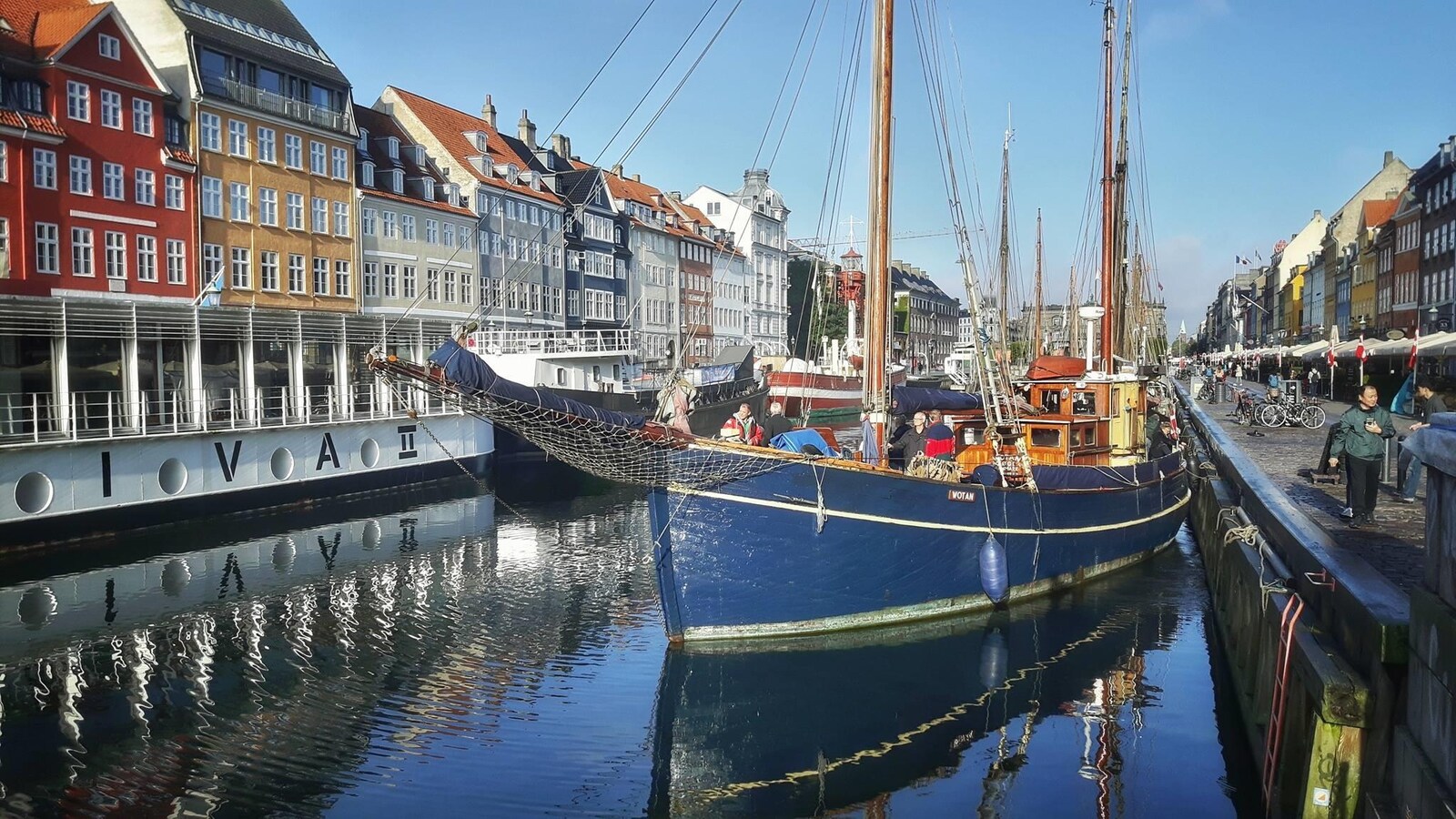 On voit un bateau bleu amarré au bord du canal, et, en arrière-plan, des façades colorées typiques de Copenhague.