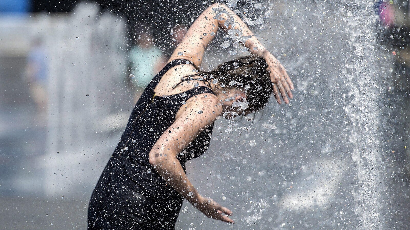 Une femme se rafraîchit dans une fontaine, à Montréal, pendant la canicule.
