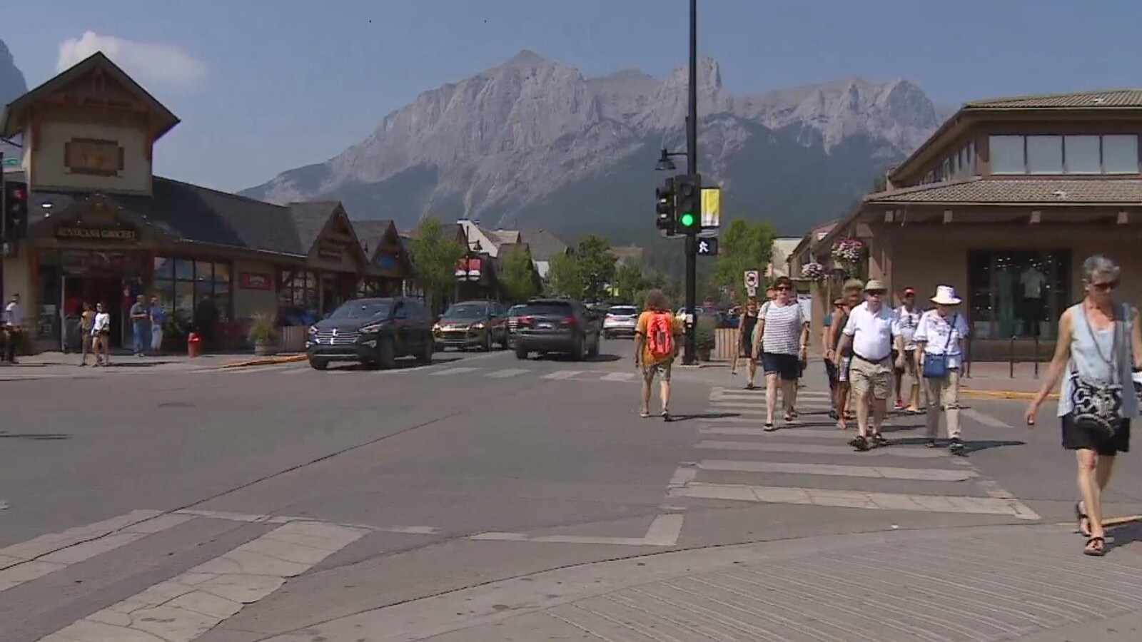 Vue sur une rue principale à Canmore. Des piétons traversent la rue et on voit les montagnes en arrière d'eux.