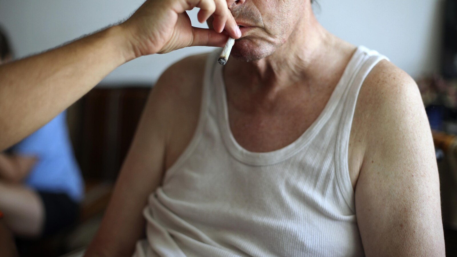 Un homme tend son bras vers la bouche d'un aîné assis pour lui donner le joint à fumer.