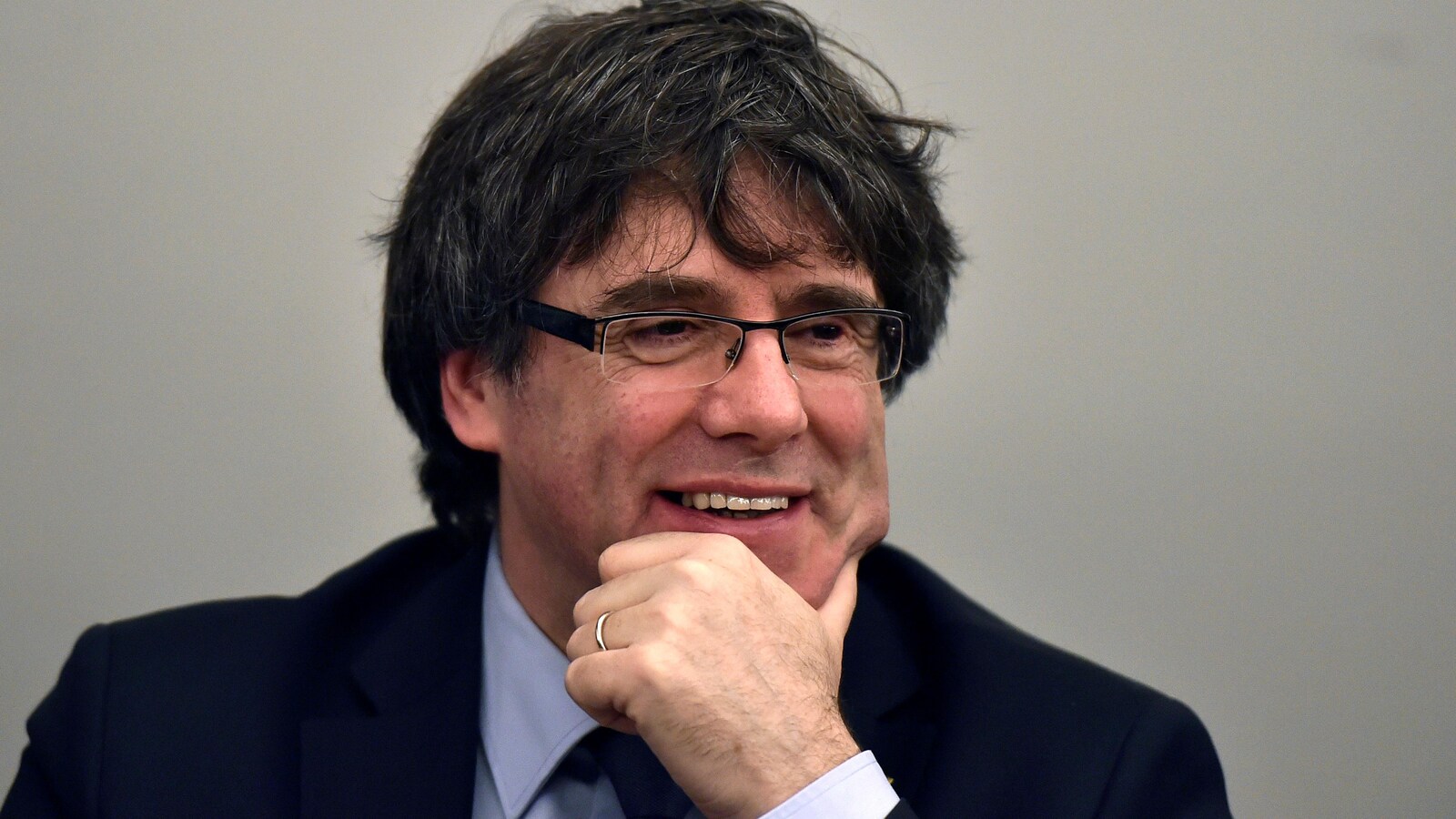 Carles Puigdemont la main au menton, esquissant un sourire.