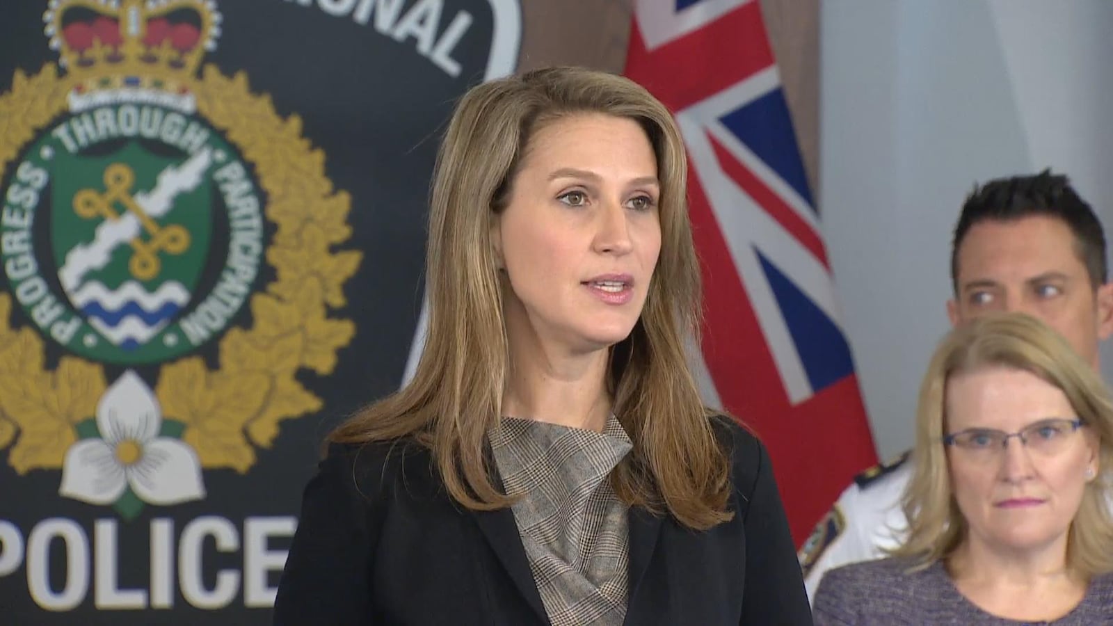 Photo d'une femme debout aux cheveux longs portant un tailleur noir devant une effigie de la police