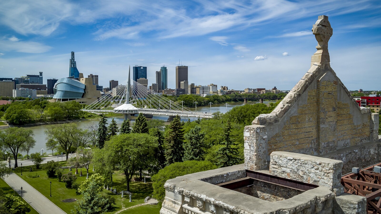 Une vue aérienne depuis les murs de pierre de l'ancienne cathédrale de Saint-Boniface, où l'on voit l'esplanade Louis-Riel, le pont Provencher, le Musée canadien pour les Droits de la personne et les immeubles de Winnipeg.