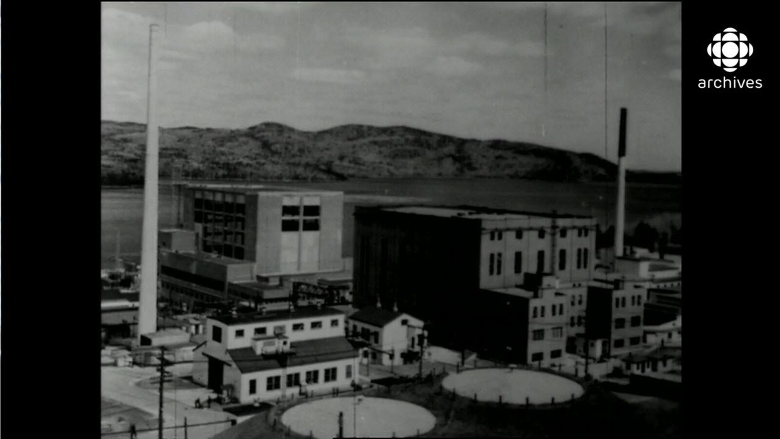 Bâtiments et longue cheminée du site de la centrale de Chalk River, avec le cours d'eau en arrière-plan