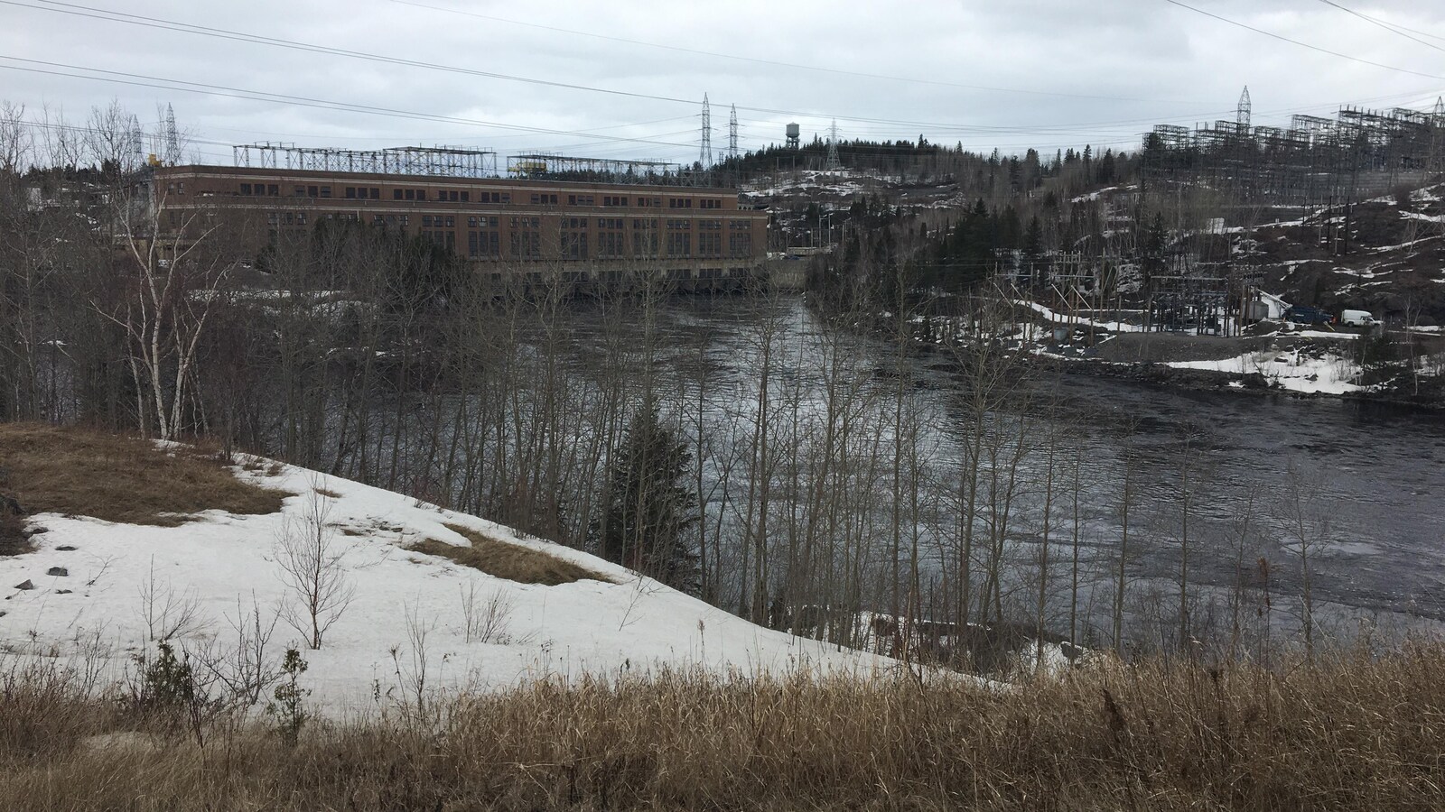 Une centrale hydroélectricité en brique. Il y a un plan d'eau entourant d'arbres et de neige.