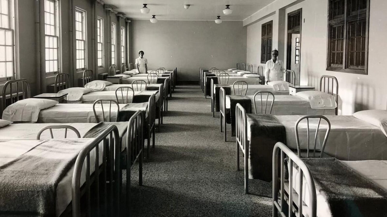 Des femmes à côté de lits dans une photo noir et blanc.