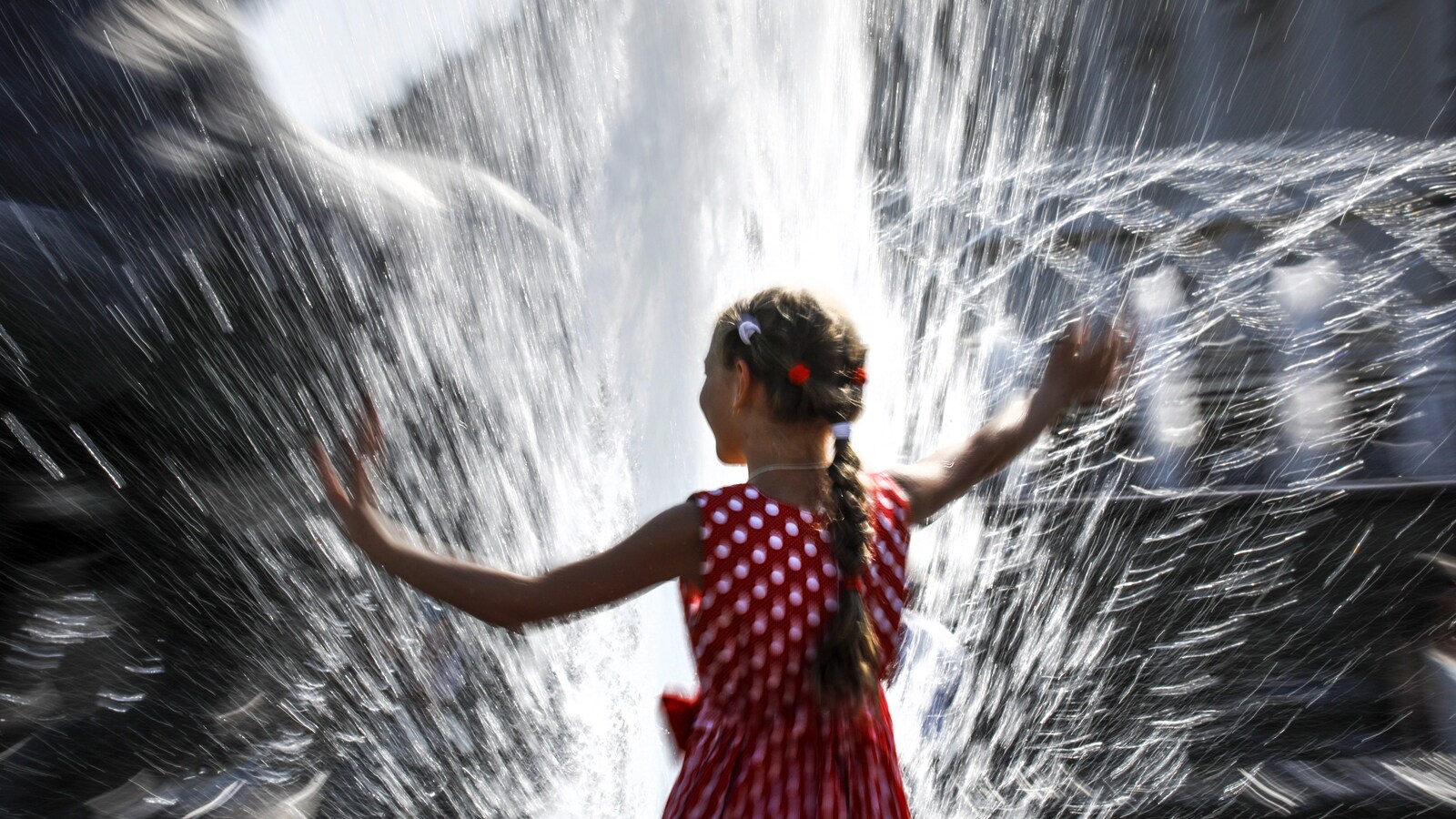 Une jeune fille avec une robe rouge à pois joue dans une fontaine d'eau.